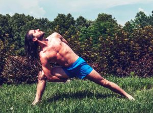 Fit Young Man with Long Hair Holding Yoga Pose in the Grass