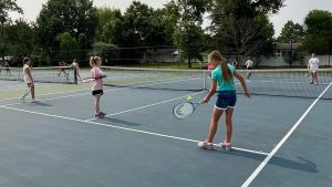 image of young girls playing tennis on a court on a summer day